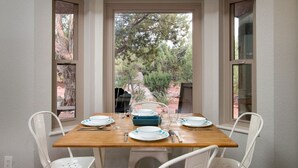 Un comedor con una mesa lista para cuatro, dos sillas a cada lado, y vistas a árboles y un edificio a través de las ventanas.
