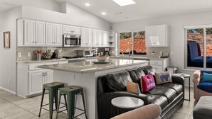 Una cocina moderna con armarios blancos, una isla central y un comedor con sofá de cuero.