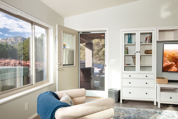 A room with a large window, a sliding glass door, a white cabinet with shelves, and a television on the wall.