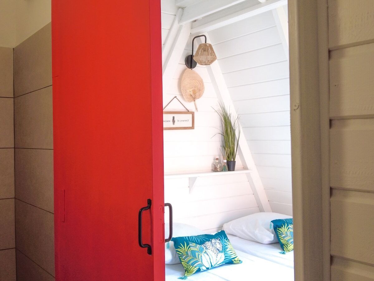 Een slaapkamer met een rode deur, een bed met blauw-witte beddengoed, een wandlamp en een ingelijste citaat.