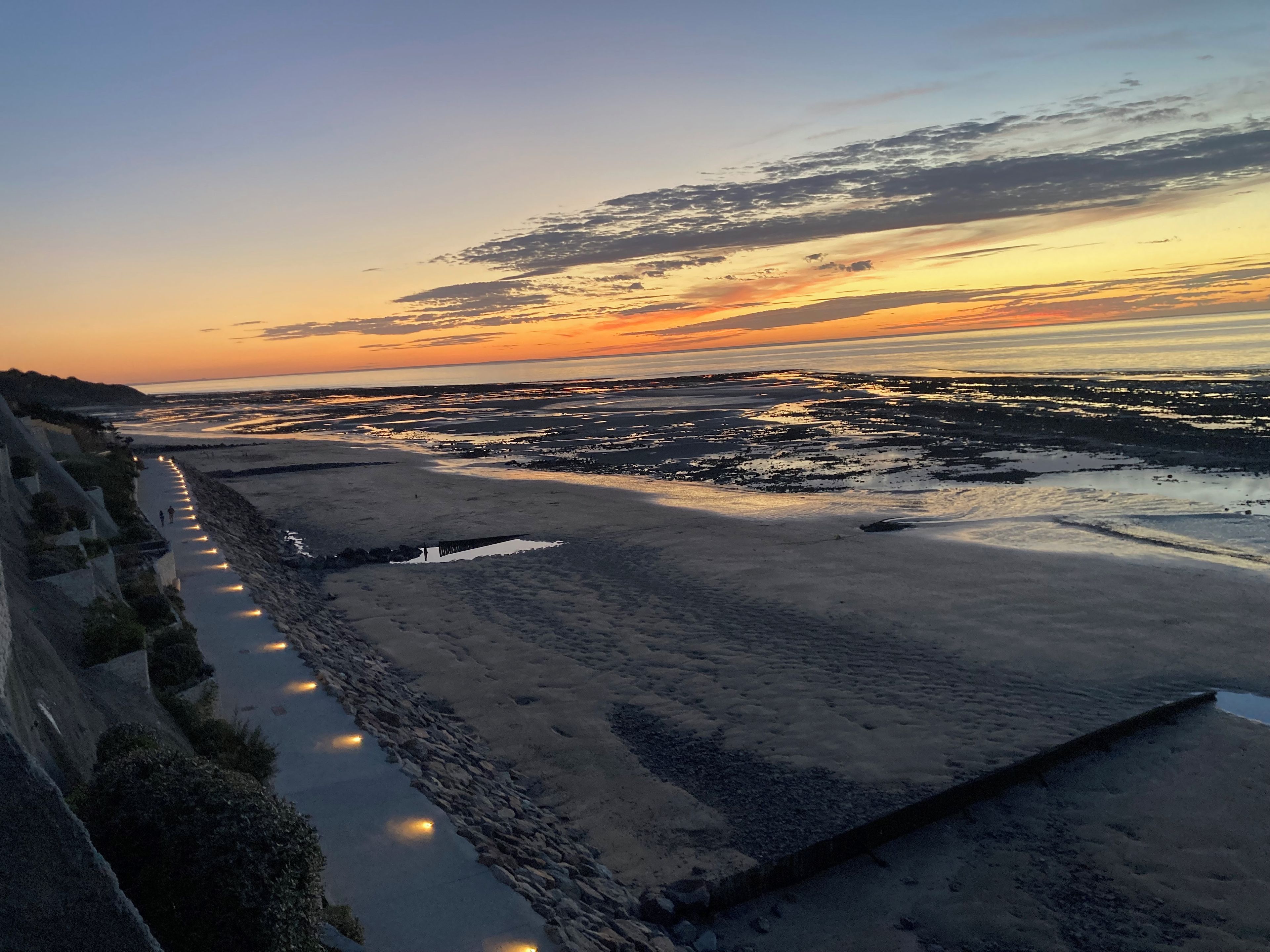 Un paisaje costero con un paseo pavimentado a lo largo de la orilla, que conduce a una zona de playa.