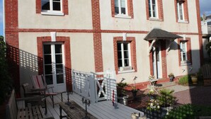 Un edificio de dos plantas con fachada roja y blanca, numerosas ventanas y un pequeño porche con mobiliario exterior.