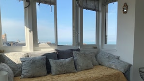 Una habitación con sofá cama, ventanas amplias, vista al mar y un tapiz de cuero de vaca.