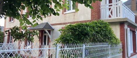 A residential building with a white fence, a small porch, and a brick chimney.