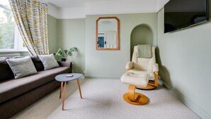 Una sala de estar moderna con un sofá, una mesita redonda, un sillón de masaje, un espejo y un televisor.