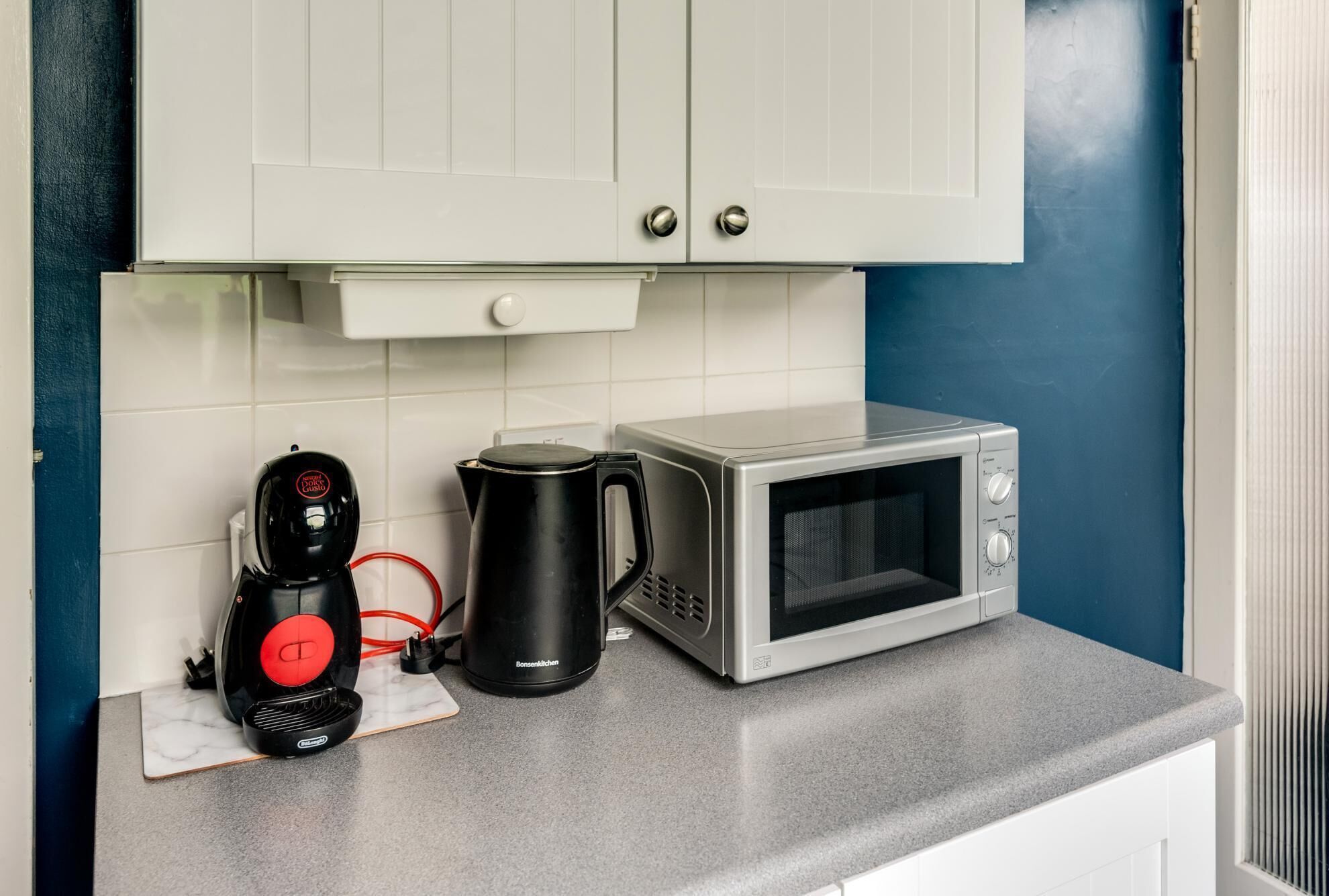 A kitchen with a microwave, a coffee maker, and a cabinet with a drawer.
