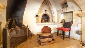 A rustic room with a stone fireplace, a woven basket, a chair with a red cushion, and a small shelf with pottery. - Archontiko Galliaki in Crete (Rethymno)