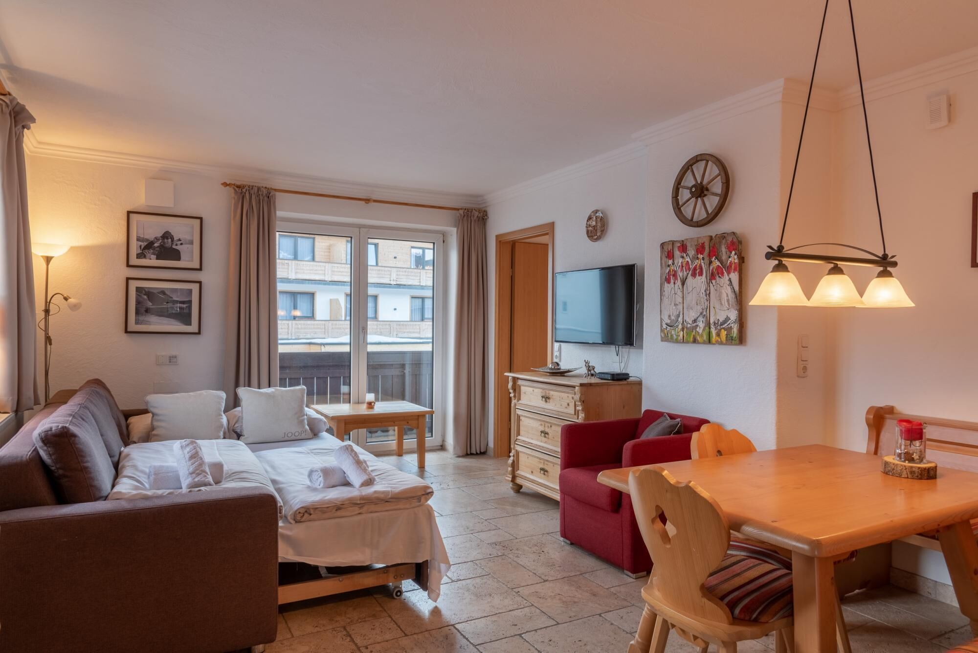 Een gemeubileerde woonkamer met een bank, een klein tafeltje, een rode fauteuil, een houten eettafel en een televisie op een houten kast.