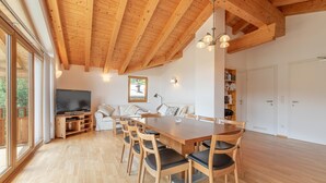 A spacious living area with a wooden dining table, chairs, a sofa, and a television.