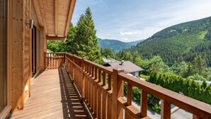 A wooden balcony with a view of a forested valley and mountains.