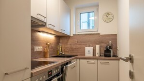 A modern kitchen with a built-in oven, a microwave, and a coffee maker. There is a window above the sink and a clock on the wall.