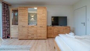 A bedroom with a wooden wardrobe, a television on a dresser, a bed with white bedding, and a stone accent wall.