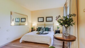 A bedroom with a large bed, a bedside table, a mirror, and a vase with flowers. - Bassotta Cottage a Charming Fairytale (Lucca)