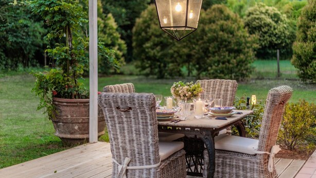 An outdoor patio with wicker furniture, a table set for dining, and a hanging lantern. - Bassotta Cottage a Charming Fairytale (Lucca)