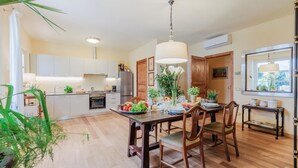 A modern kitchen with wooden cabinets, a dining table set for four, and a large window with a view of greenery. - Bassotta Cottage a Charming Fairytale (Lucca)