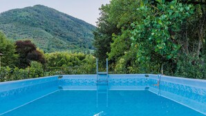 A rectangular pool with a clear blue water surface, surrounded by lush greenery and a mountain in the background. - Bassotta Cottage a Charming Fairytale (Lucca)