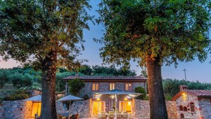 A stone house with a patio, two large trees, and a well-lit outdoor seating area. - Nonno Giulivo Farmhouse Tuscan Sanctuary (Capannori)