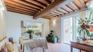 A dining area with a table set for four, a wooden ceiling, and a view of the kitchen and outside. - Nonno Giulivo Farmhouse Tuscan Sanctuary (Capannori)