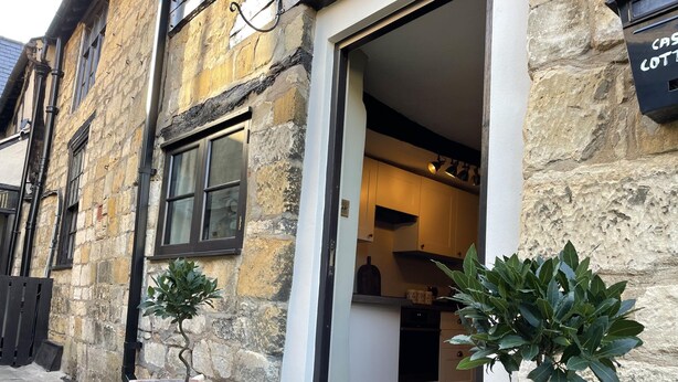 A stone building with a visible entrance, a potted plant, and a sign indicating a cottage. - Cotswold Cottage in Winchcombe Near Broadway (Cheltenham)