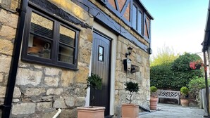 A stone building with a dark wooden door, a window with shutters, and a small potted plant in front. - Cotswold Cottage in Winchcombe Near Broadway (Cheltenham)