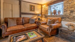 A cozy living room with leather sofas, a coffee table, and a stone wall. - Cotswold Cottage in Winchcombe Near Broadway (Cheltenham)