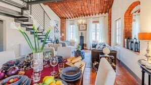 A dining area with a wooden table set for a meal, surrounded by sofas and a staircase. - Casa Lucky a Modern Lucca Penthouse (Lucca)