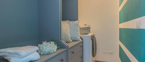 A modern bathroom with a grey vanity, a white towel stack, a white flower arrangement, and a washing machine.