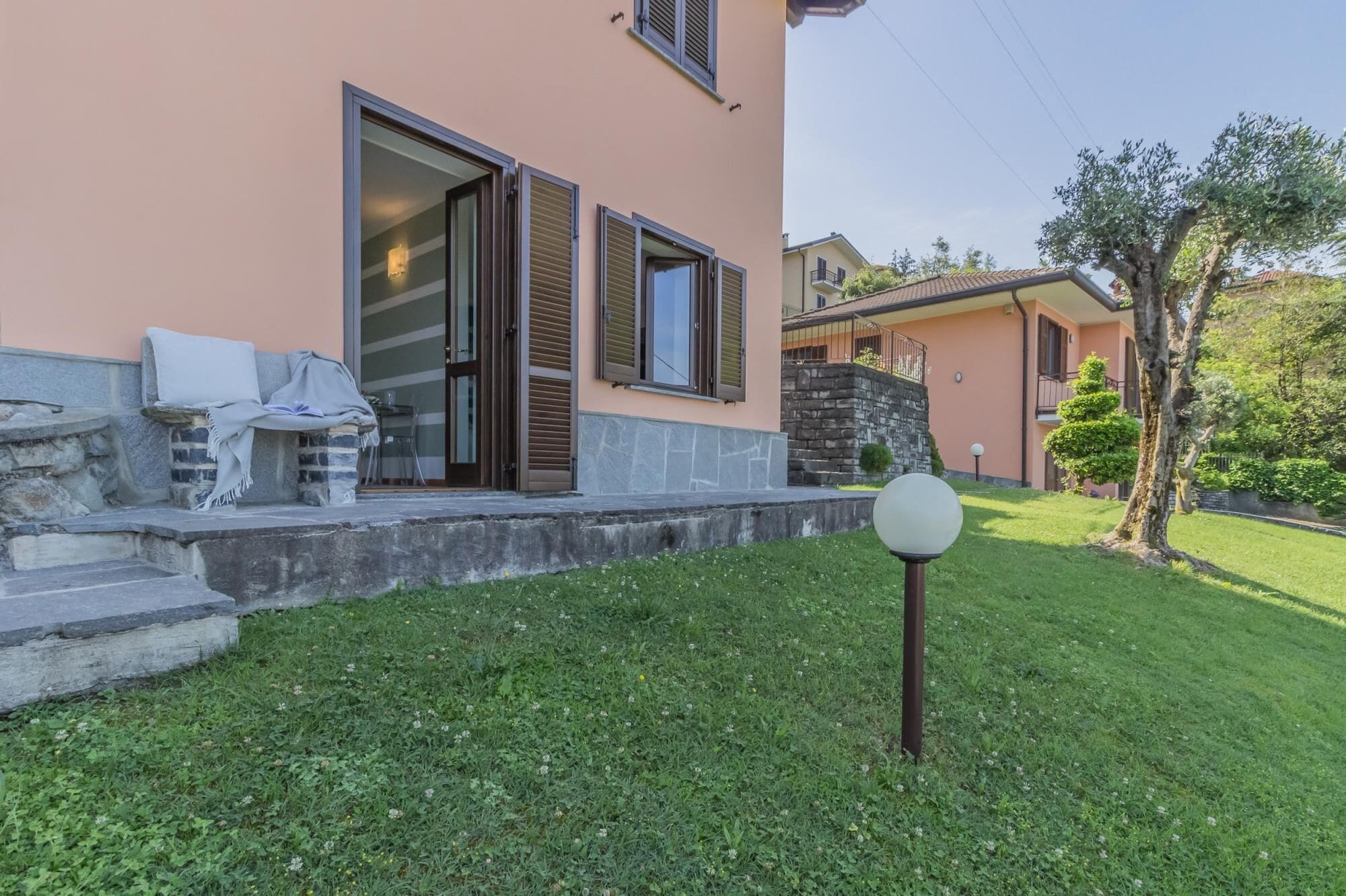 A modern house with a stone staircase, a covered outdoor seating area, and a well-maintained lawn.