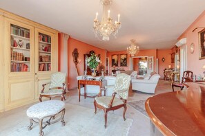 Un vaste salon agrémenté d’un canapé blanc, d’une table basse en bois et d’un lustre. On y trouve des étagères remplies de livres et d’objets décoratifs.