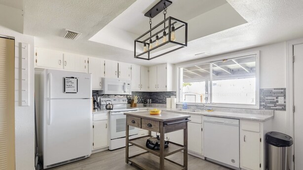 A modern kitchen with white cabinets, a central island, a built-in oven, and a window with a view. - Cozy 3 bed 2 baths in middle Glendale (Phoenix)