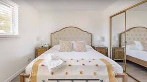A neatly made bed with floral pillows, a bedside table with a lamp, and a large mirror. - Cozy 3 bed 2 baths in middle Glendale (Phoenix)