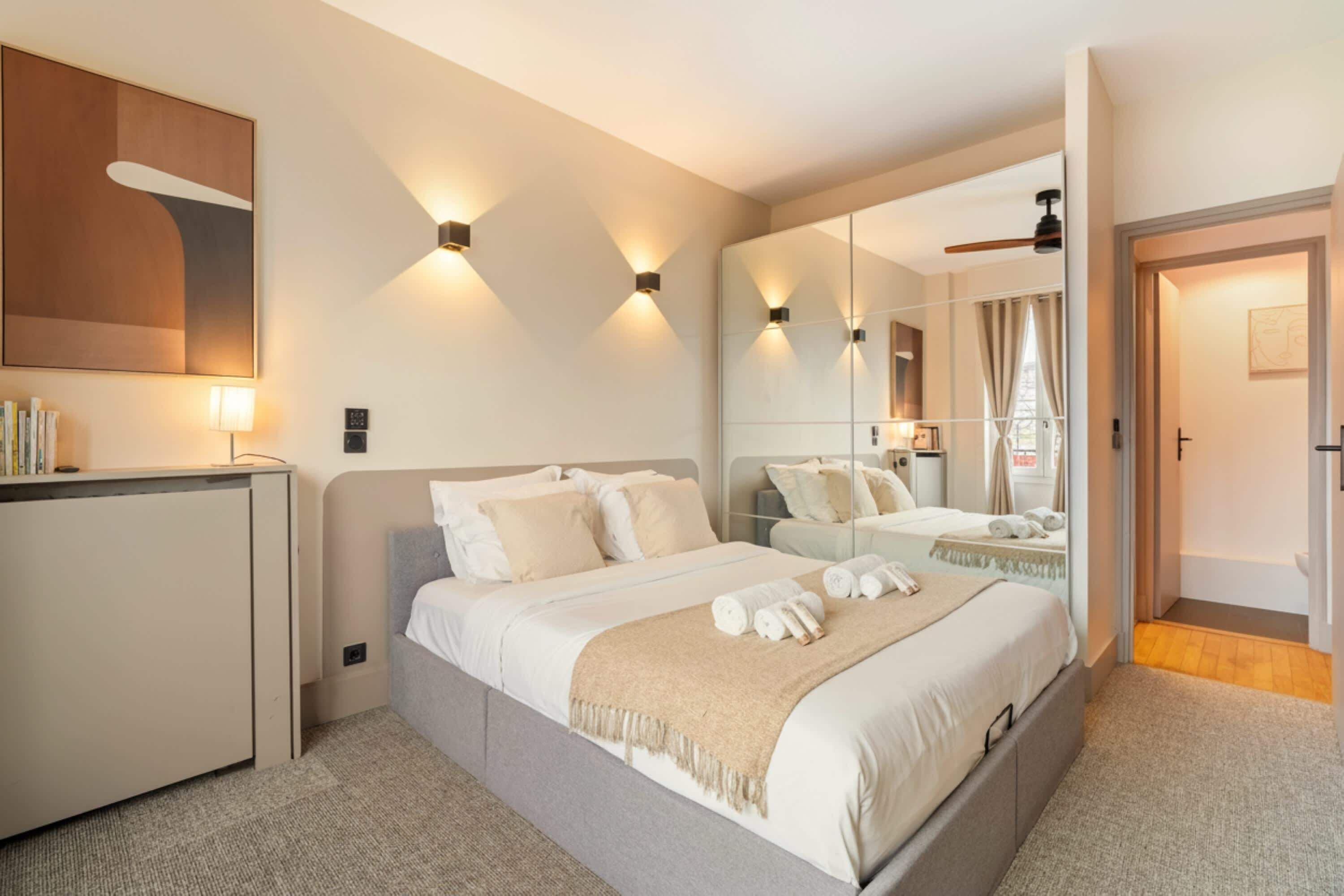 A modern hotel room with a large bed, bedside tables, a desk, and a mirror.