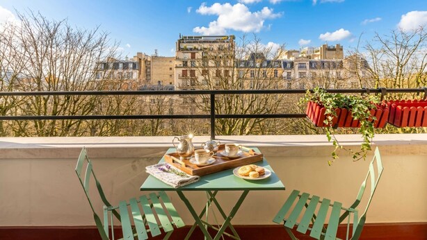 A balcony with a table set for tea, a view of buildings, and a railing.