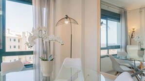Una habitación de hotel moderna con una mesa de vidrio, sillas blancas, una orquídea en maceta y una lámpara de pie.