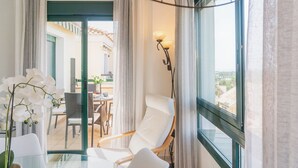 Una habitación moderna con una mesa de vidrio, sillas blancas, una orquídea en maceta y vistas a un balcón exterior con zona de comedor.