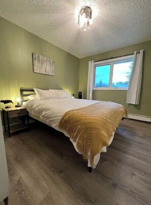 A bedroom with a bed, a nightstand, a window, and a ceiling light fixture.