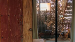 A room with a large bed, a sliding glass door leading to an outdoor area with a table and chairs, and a wooden door. - Boulenc Bed and Bread (Oaxaca)