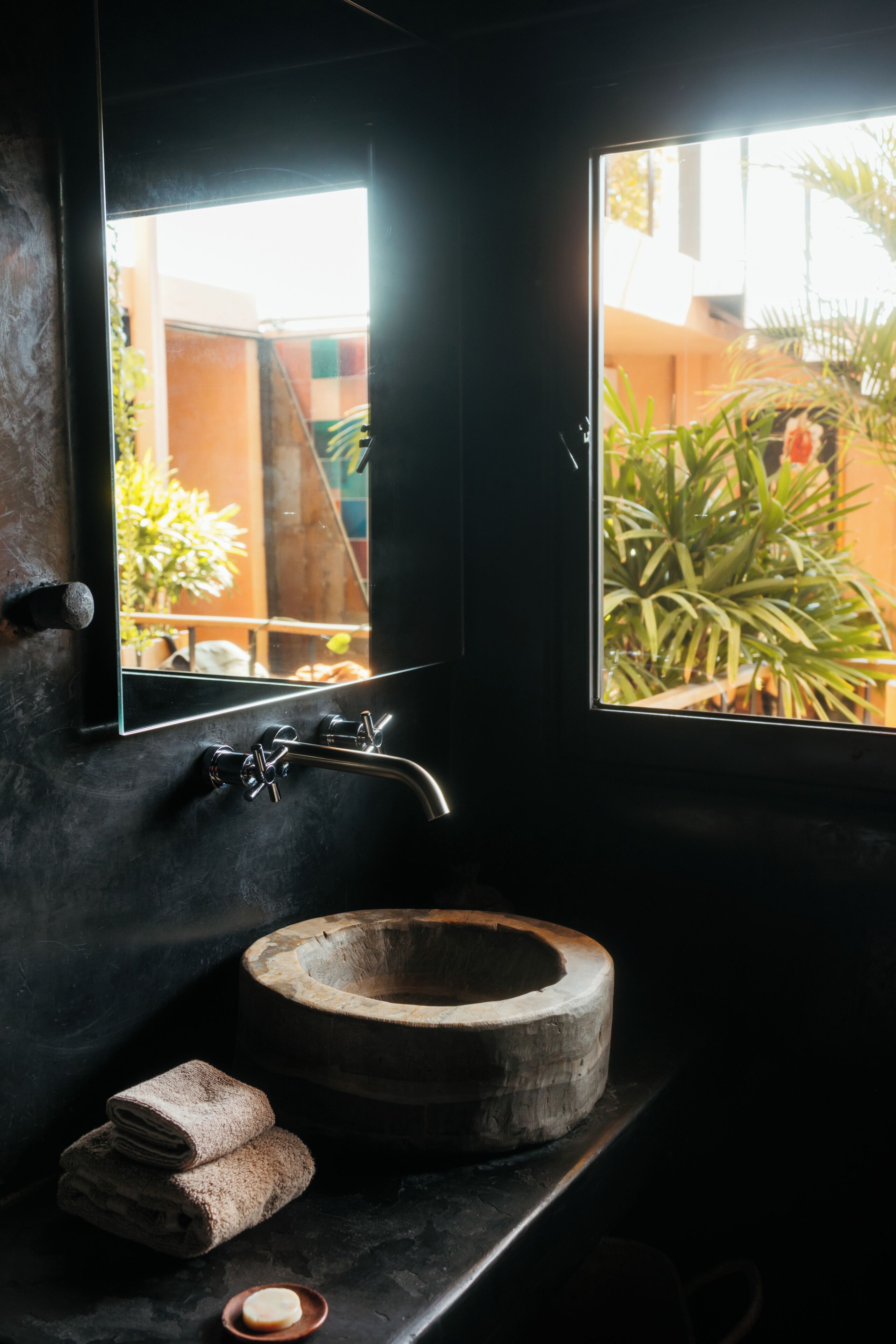 A bathroom with a wooden sink, a mirror, and a window with a view of a courtyard.