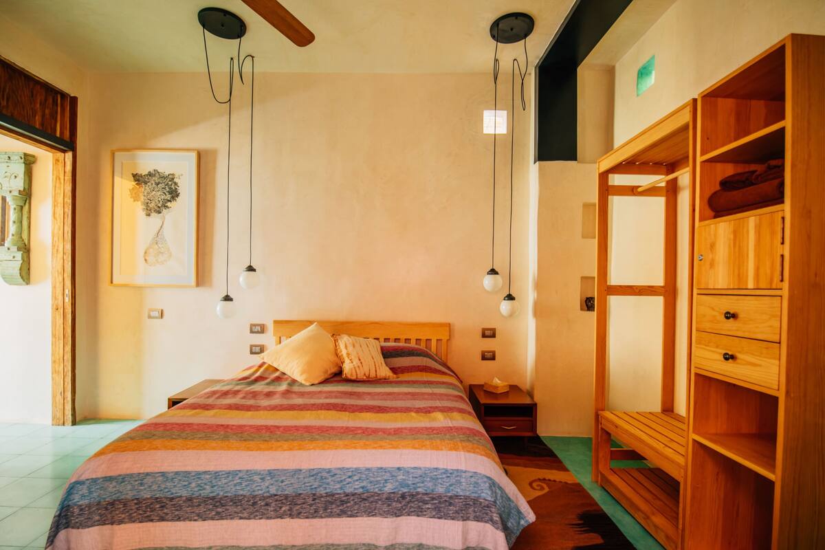 A bedroom with a wooden bed, a nightstand, a dresser, and hanging pendant lights.