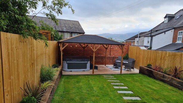 Un patio trasero con un jacuzzi, una pérgola de madera y un camino de piedra.