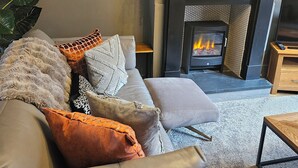 Una sala de estar moderna con chimenea, un sofá con varios cojines y un televisor sobre un soporte de madera.