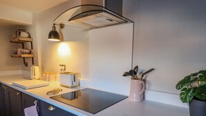Cocina moderna con encimera negra, horno empotrado, tostadora y una taza rosa con utensilios.
