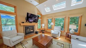 Un salón amplio con chimenea, asientos cómodos y ventanas grandes con vistas al exterior.