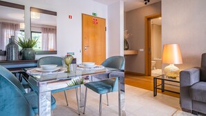Ein modernes Hotelzimmer mit einem Glastisch, zwei blauen Stühlen, einer Couch, einer Lampe und einem Spiegel.