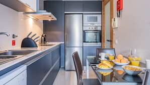Eine moderne Küche mit Kühlschrank, Backofen und Mikrowelle. Ein Esstisch mit Frühstücksangeboten und ein Stuhl sind ebenfalls vorhanden.