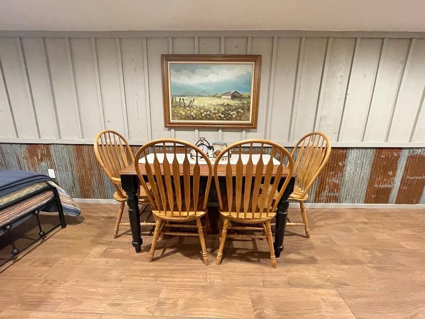 Un comedor con una mesa y sillas de madera, un cuadro enmarcado en la pared y un suelo de madera rústica.