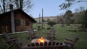 Una baita rustica con un braciere al centro, circondata da poltrone Adirondack.
