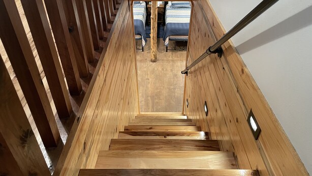 Una scala in legno con ringhiera che conduce a una stanza con un letto e un comodino.