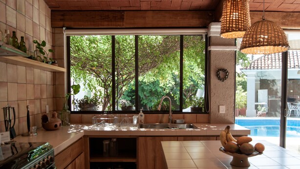 A kitchen with a large window, wooden cabinets, a sink, and a fruit bowl on the counter. - Casa Quinta Mar Casa de campo en el Tule (Santa Maria del Tule)