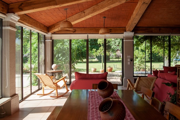 A spacious room with large windows, a wooden ceiling, and a dining area with a table and chairs.